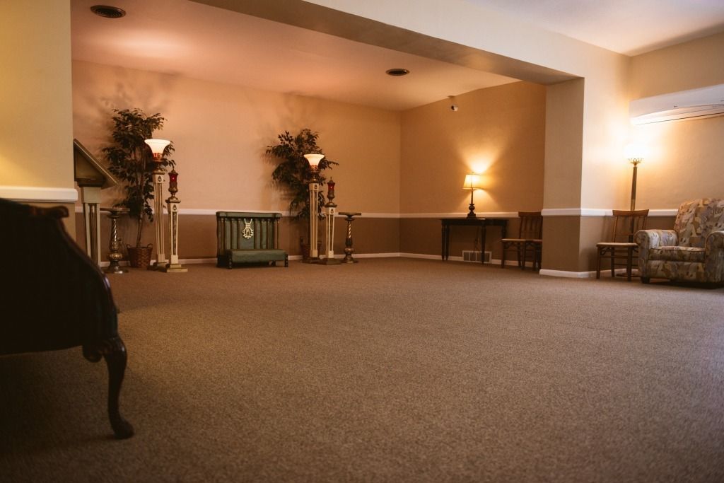 Empty carpeted banquet hall with warm lighting, tables, and decorative plants along the walls