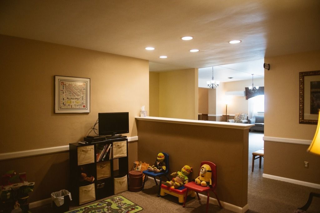 Basement playroom with toys, TV, couch, and warm recessed lighting