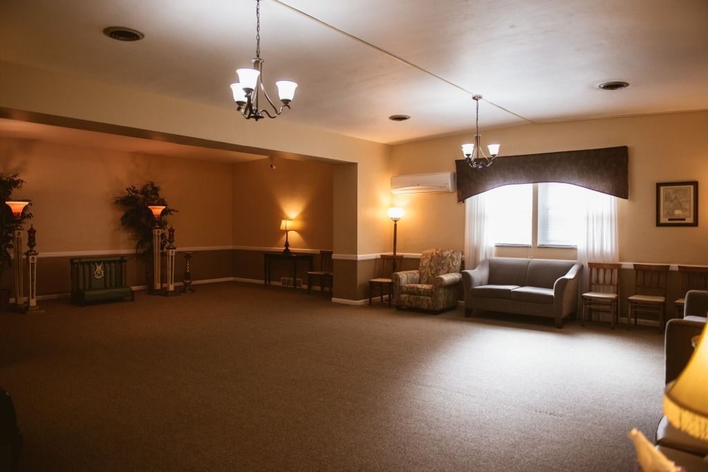 Empty waiting room with brown carpet, sofas, chairs, and warm ceiling lights near a bright window