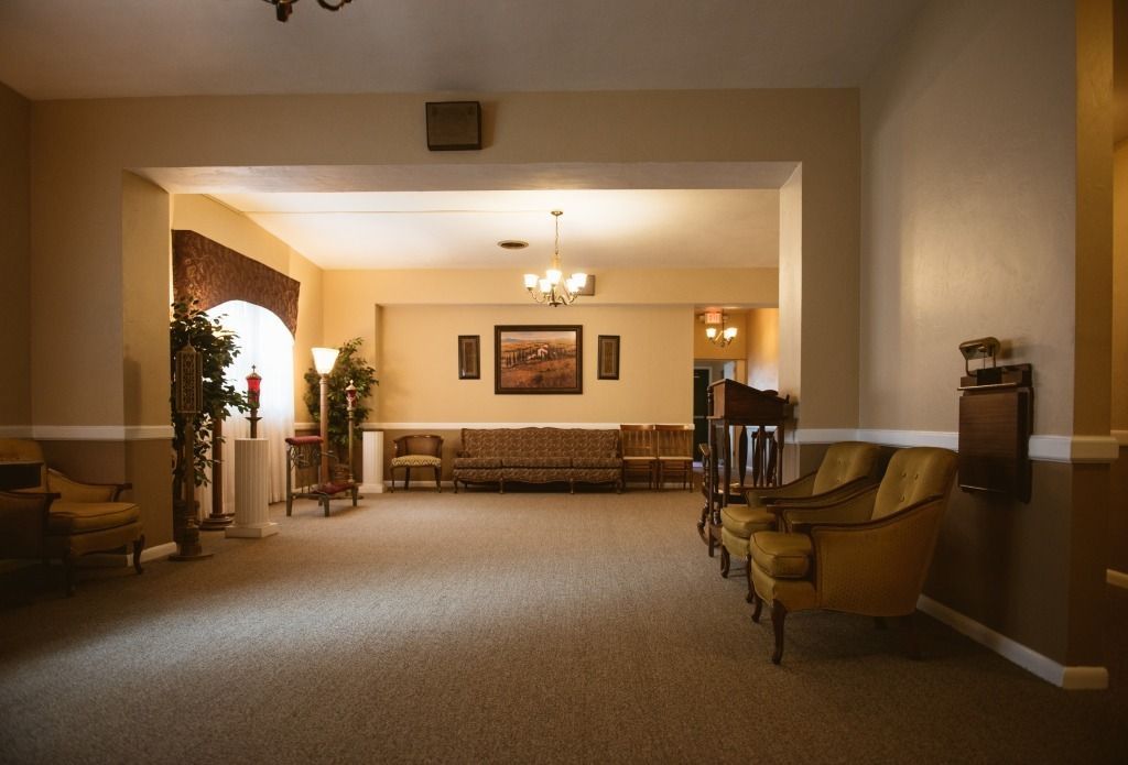 Dim hotel lobby with beige carpet, chandeliers, sofas, and armchairs in a quiet waiting area