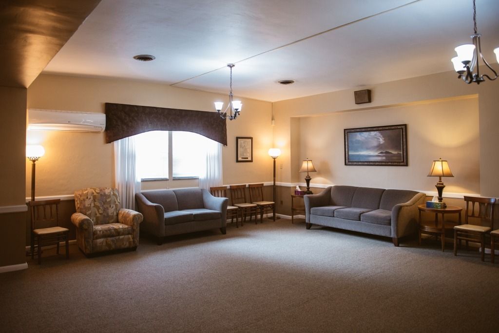 Spacious waiting room with sofas, chairs, lamps, and a large window under warm lighting