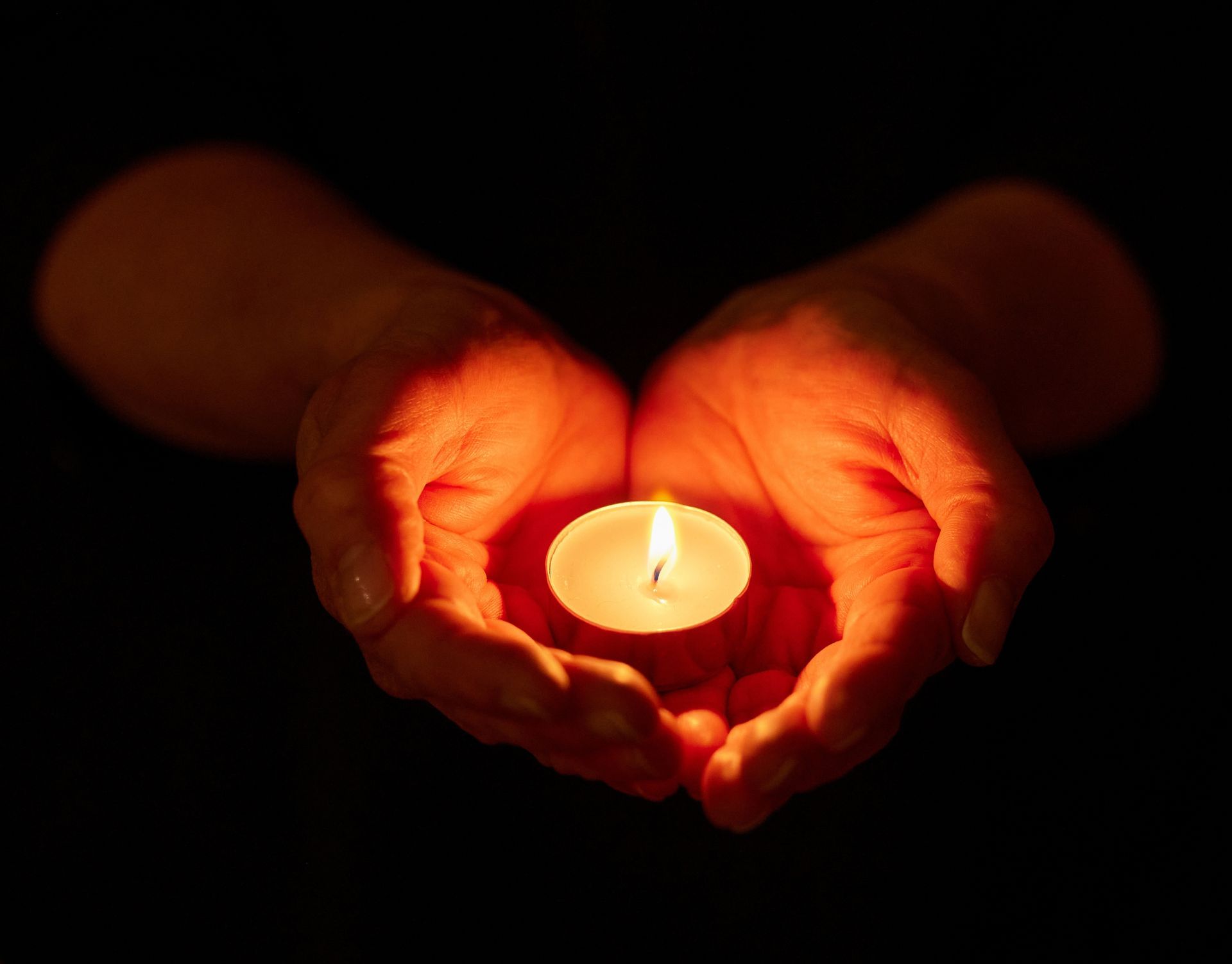 Hands cupping a lit candle in the dark