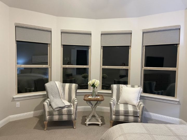 A bedroom with two chairs and a table in it, the windows have child safe cordless blinds.