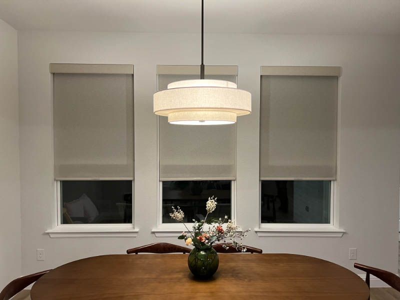 Love is Blinds CO: a vase of flowers is on the table in the dining room with roller shades on the windows.