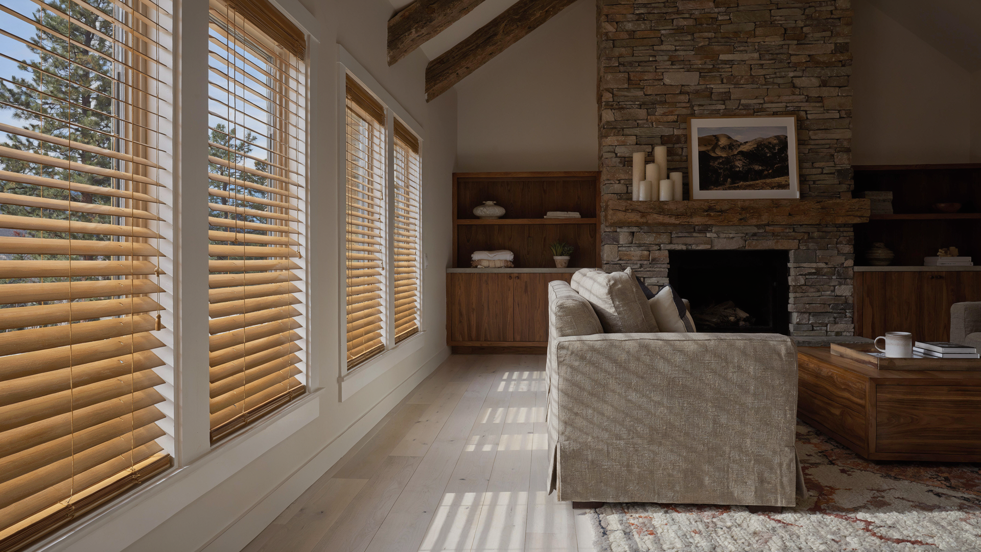 Sunlit living room with wood blinds, fireplace, beige sofa, and brick accent wall