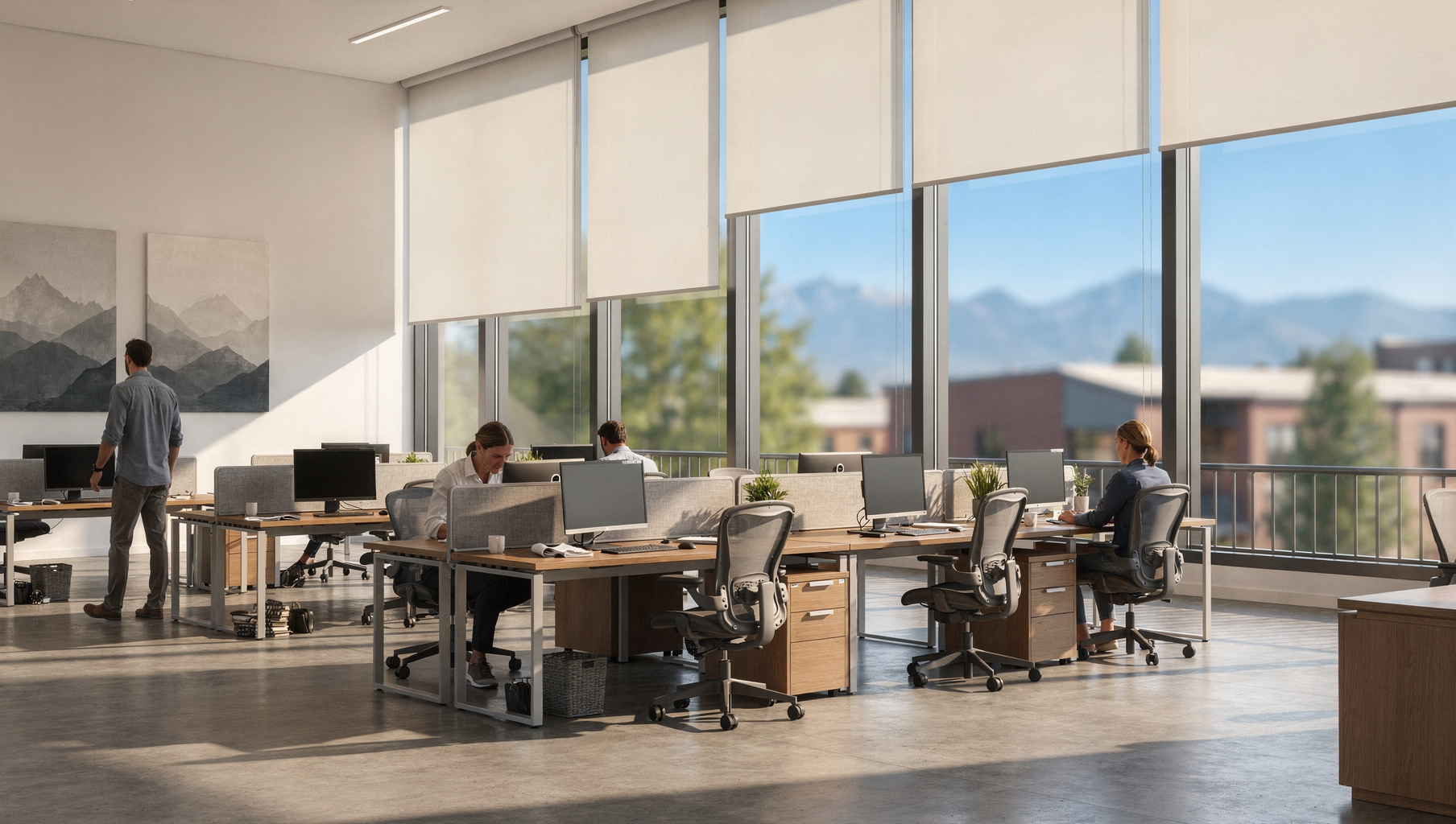 Bright open office with coworkers at desks, large windows with solar shades, and mountain views.