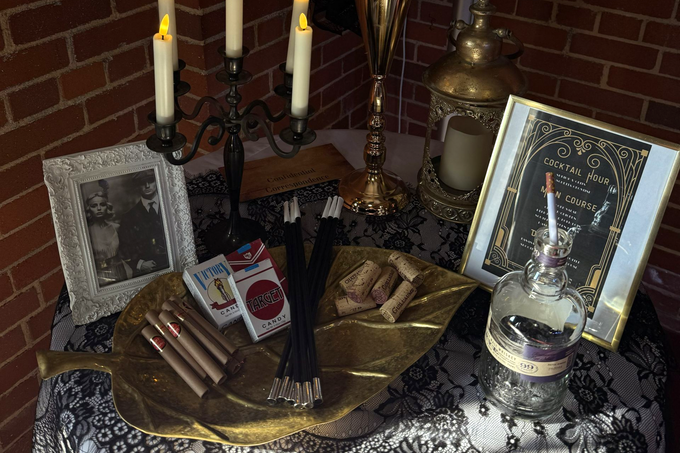 Halloween altar with candles, a pentagram tray, tarot cards, skulls, and framed occult images on a table