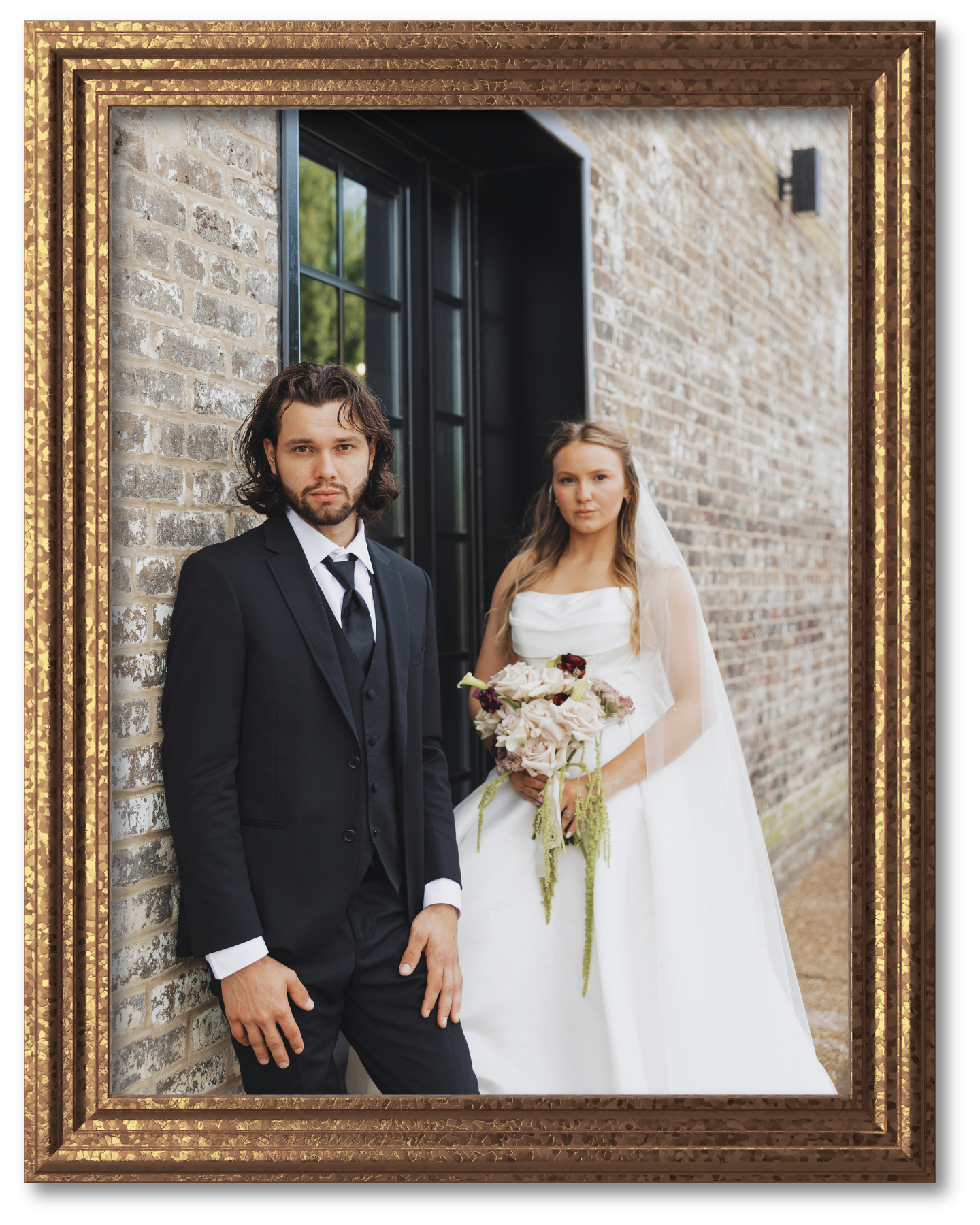Bride and groom standing outdoors beside a stone building, bride holding a bouquet in a white dress and veil