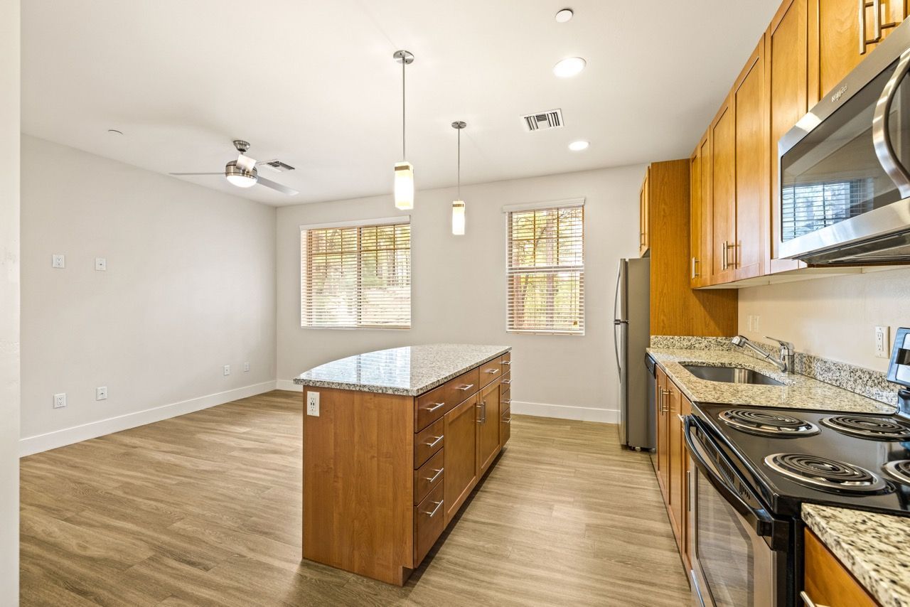 Open kitchen in a rental with an island, granite counters, wood cabinets, and stainless appliances.