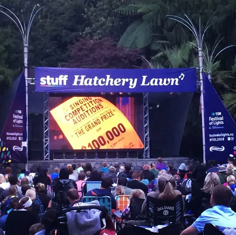 A crowd of people are sitting under a banner that says stuff hatchery lawn