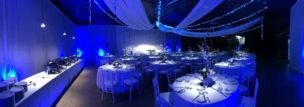 A large room with tables and chairs set up for a party with blue lights.