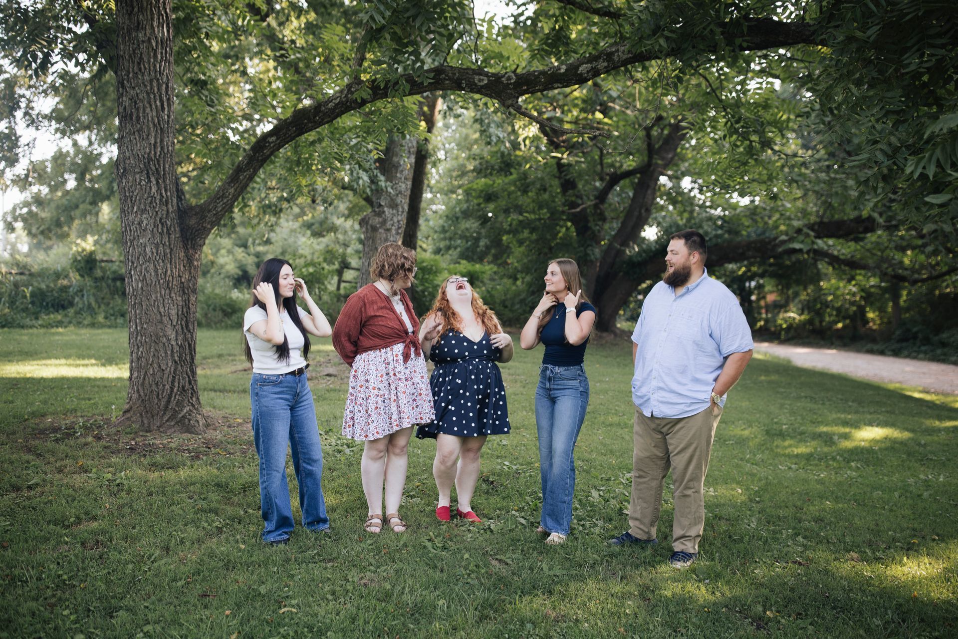 Five people standing and chatting in a grassy park under trees