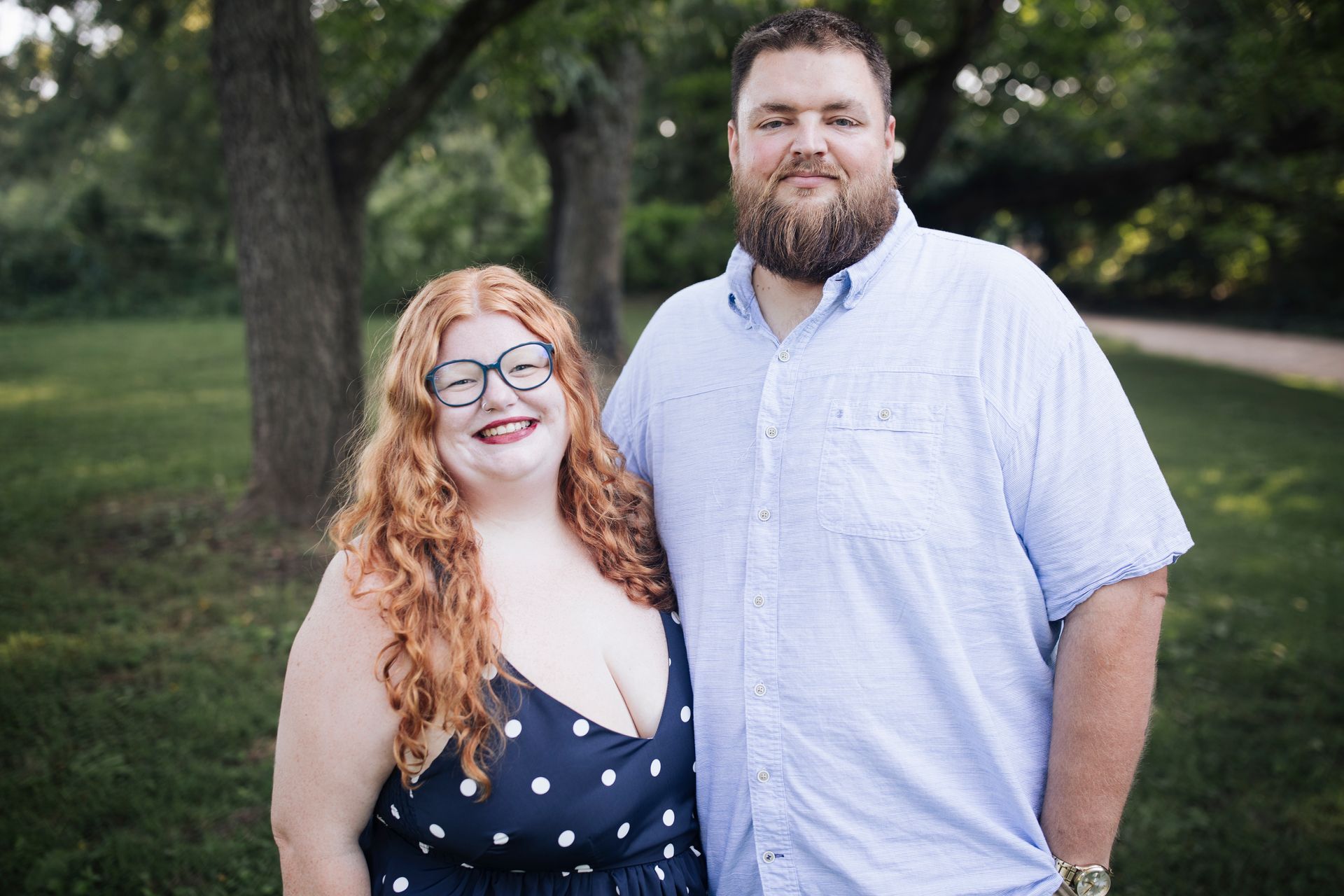 Two smiling adults standing together outdoors, one in a navy patterned dress and the other in a light blue shirt.