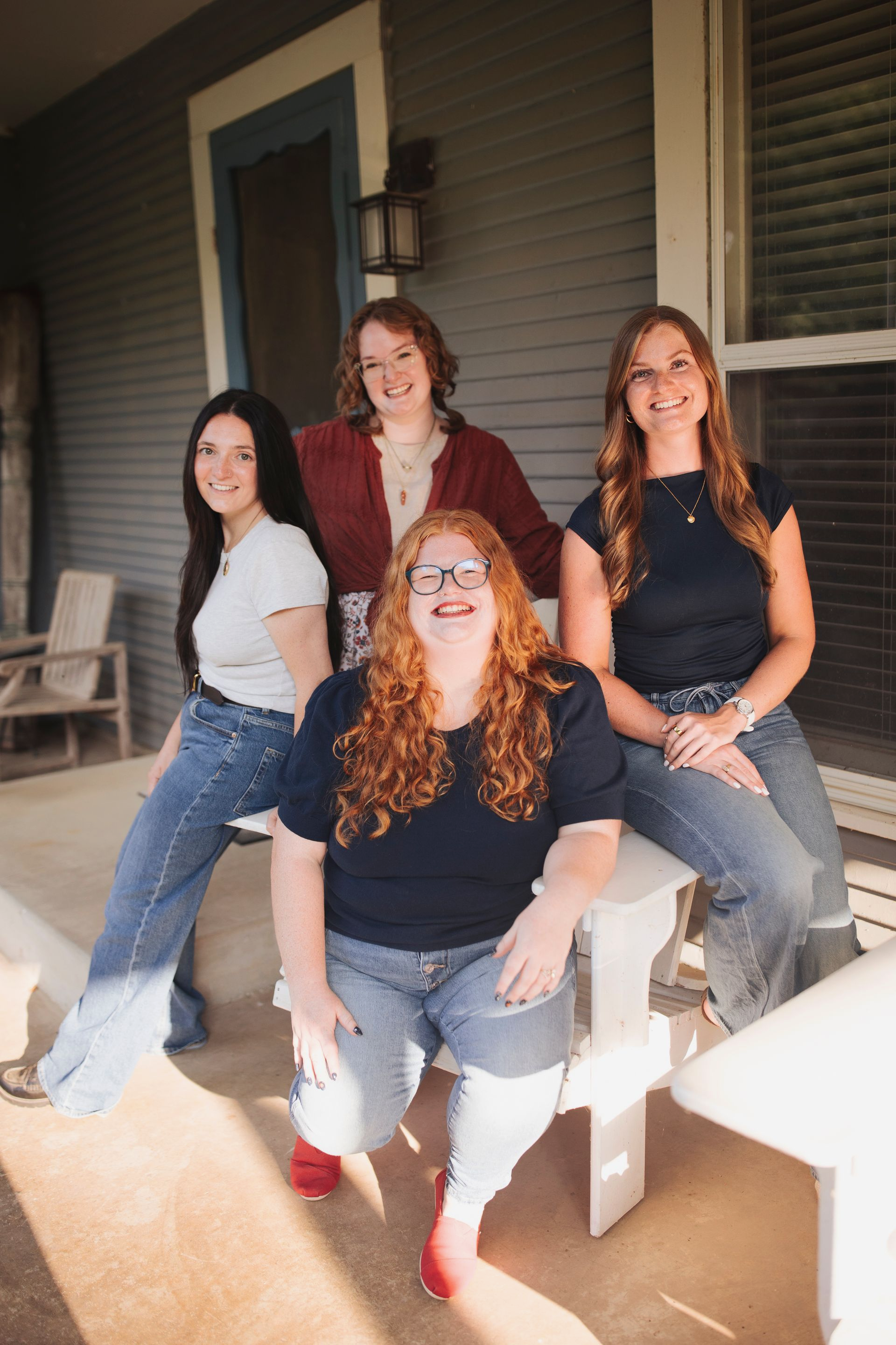 Four people sitting and posing on a porch, smiling in casual clothes.