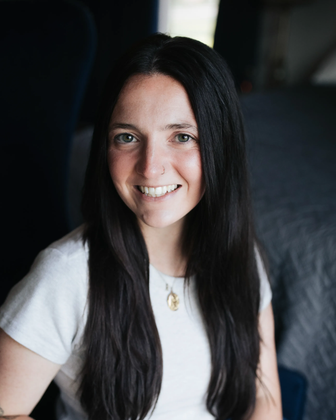 Smiling woman with long dark hair wearing a white shirt in a dim indoor setting