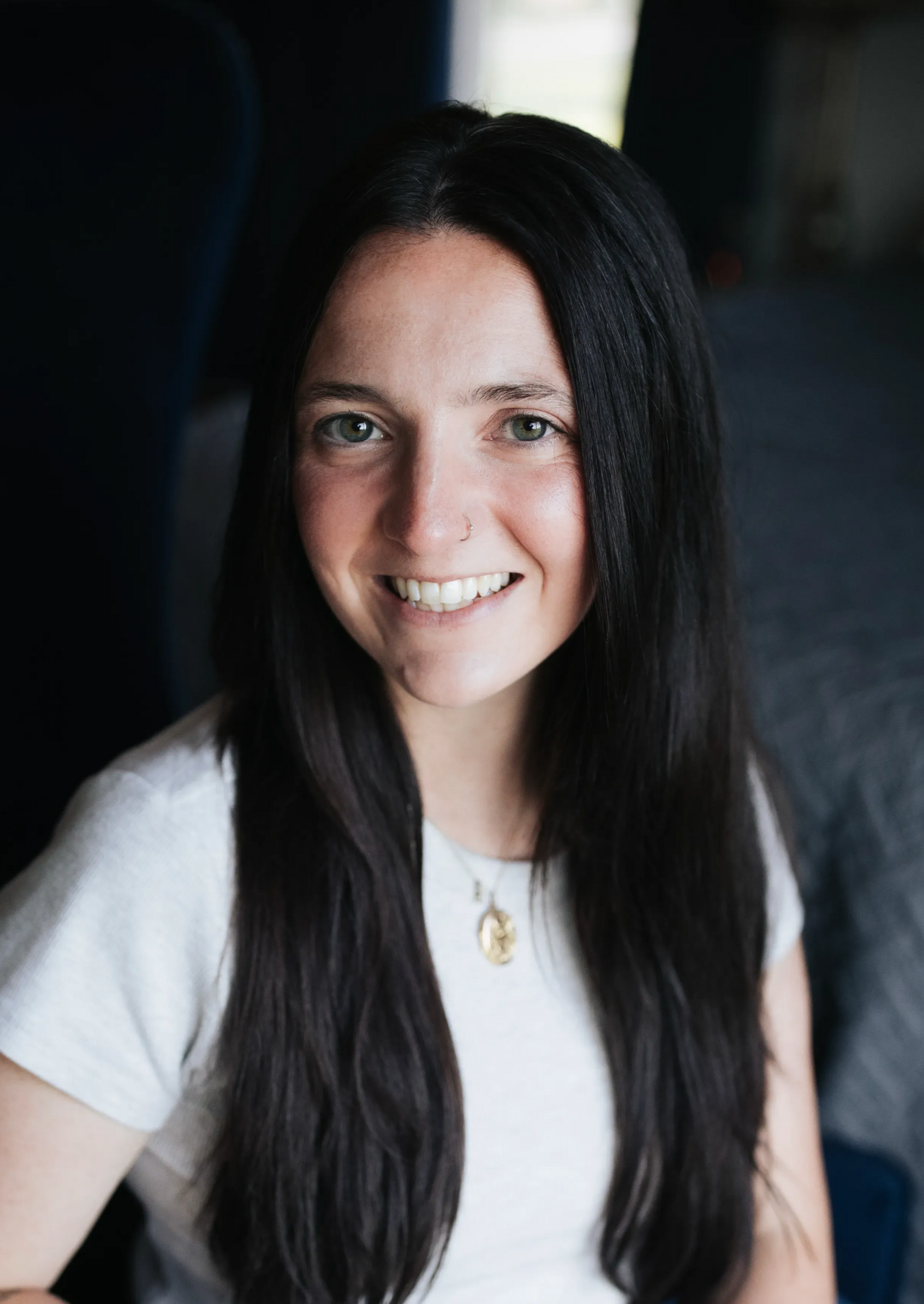 Smiling woman with long dark hair wearing a white shirt in a dim indoor setting
