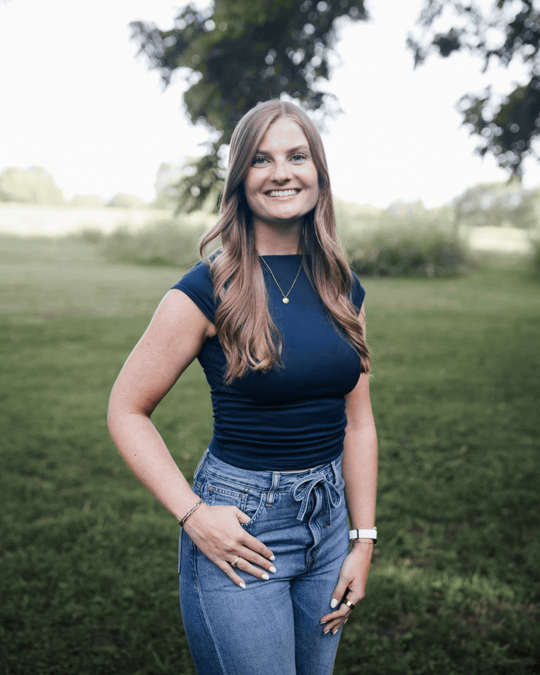 Woman standing outdoors on grass, smiling in a navy top and jeans.