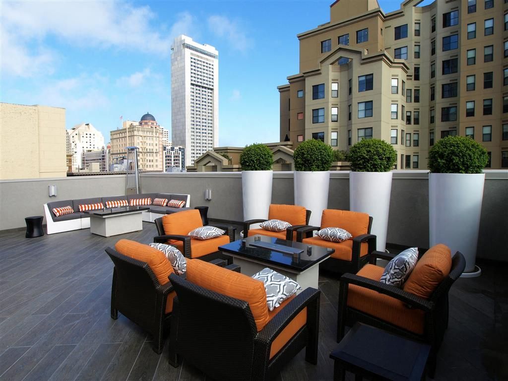 Rooftop community terrace with orange-cushioned lounge seating and planters, city skyline in background at Tower 737, offering apartments in San Francisco, CA.