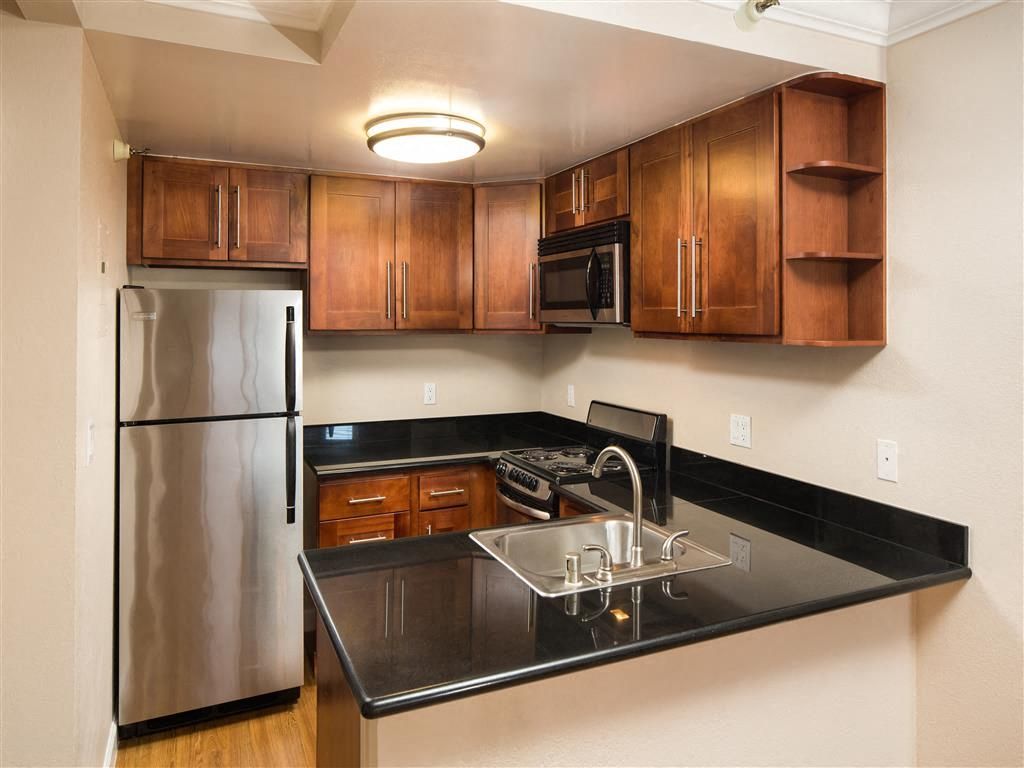 Compact apartment kitchen with dark granite counters, stainless steel appliances, and wooden cabinets at Tower 737, offering apartments in San Francisco, CA.