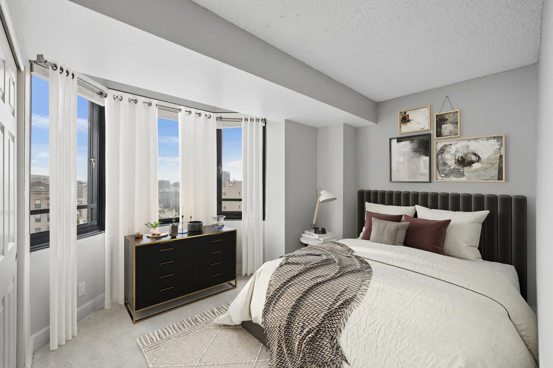 Modern bedroom in an apartment with large windows, sheer white curtains, a dark upholstered headboard, and a dresser at Tower 737, offering apartments in San Francisco, CA.