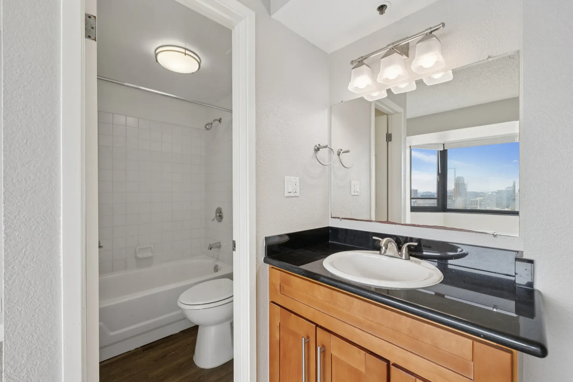 Bathroom vanity with black countertop, sink, and large mirror; tub/shower on left at Tower 737, offering apartments in San Francisco, CA.