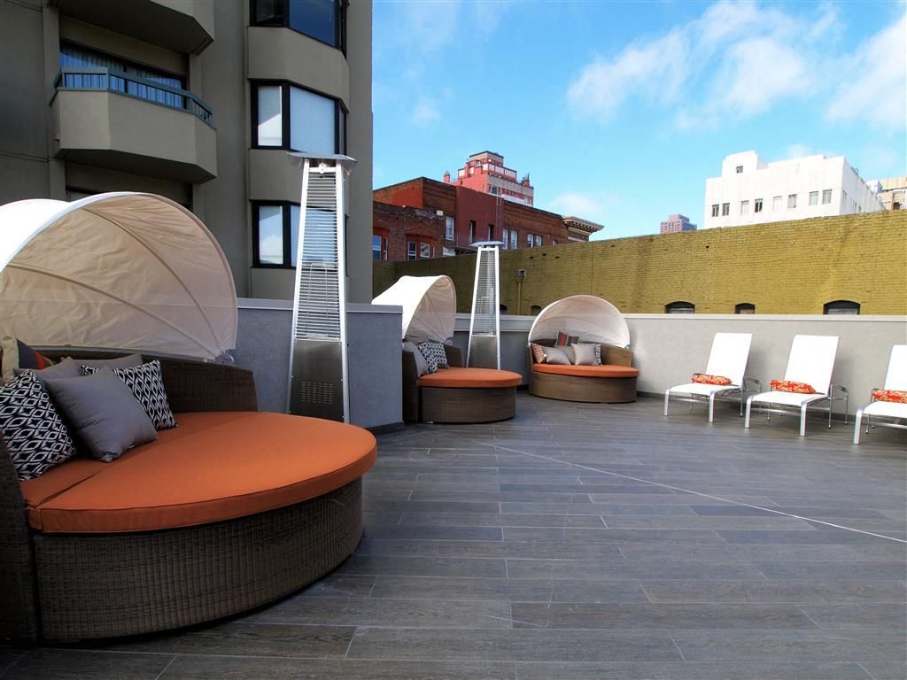 Rooftop terrace with curved wicker couches, orange cushions, and white sun loungers at Tower 737, offering apartments in San Francisco, CA.