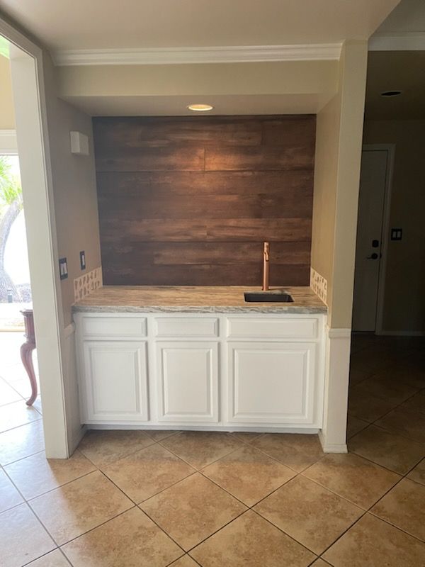 A kitchen with white cabinets , a sink , and a wooden wall.