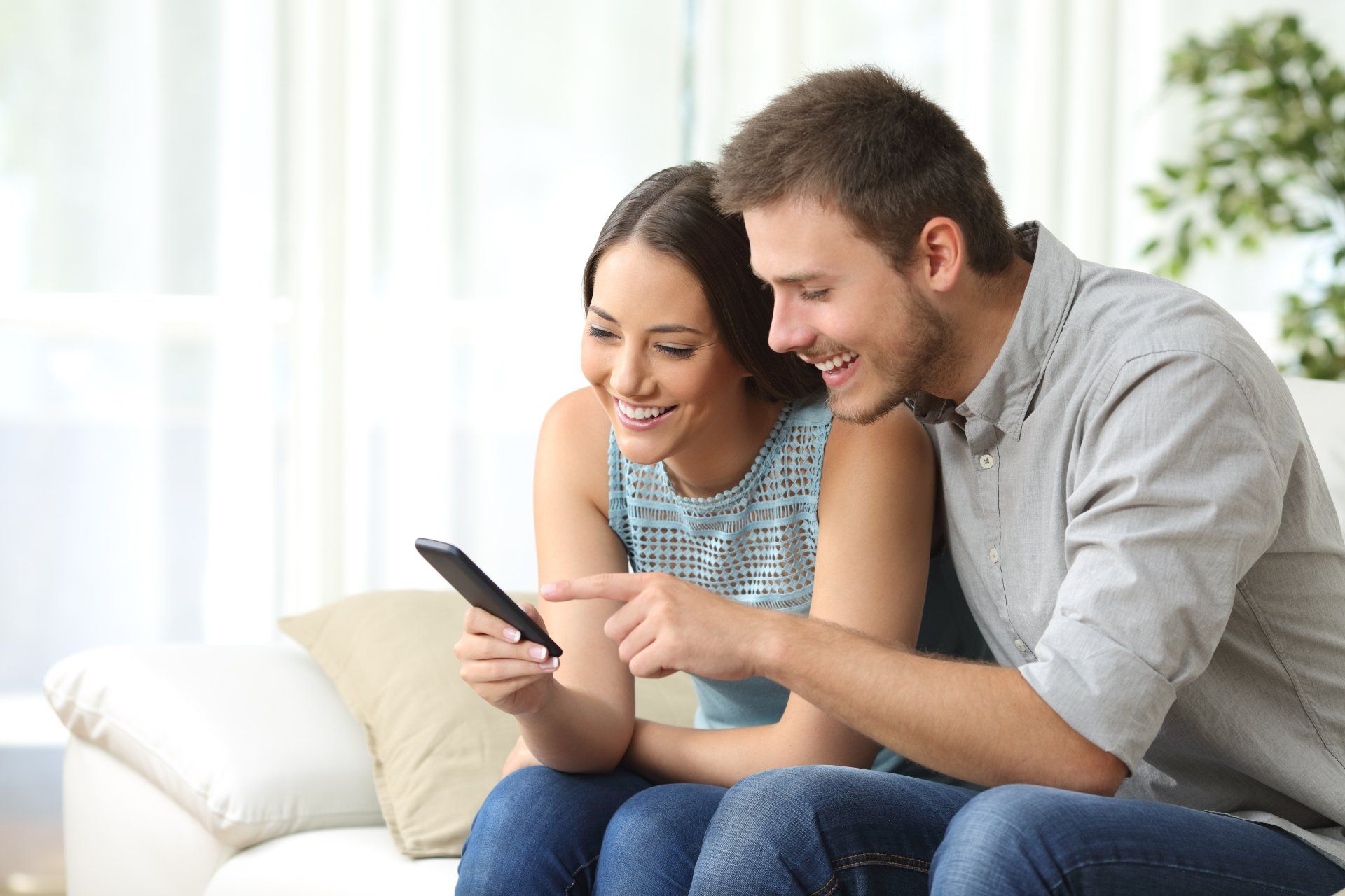 A man and a woman are sitting on a couch looking at a cell phone.