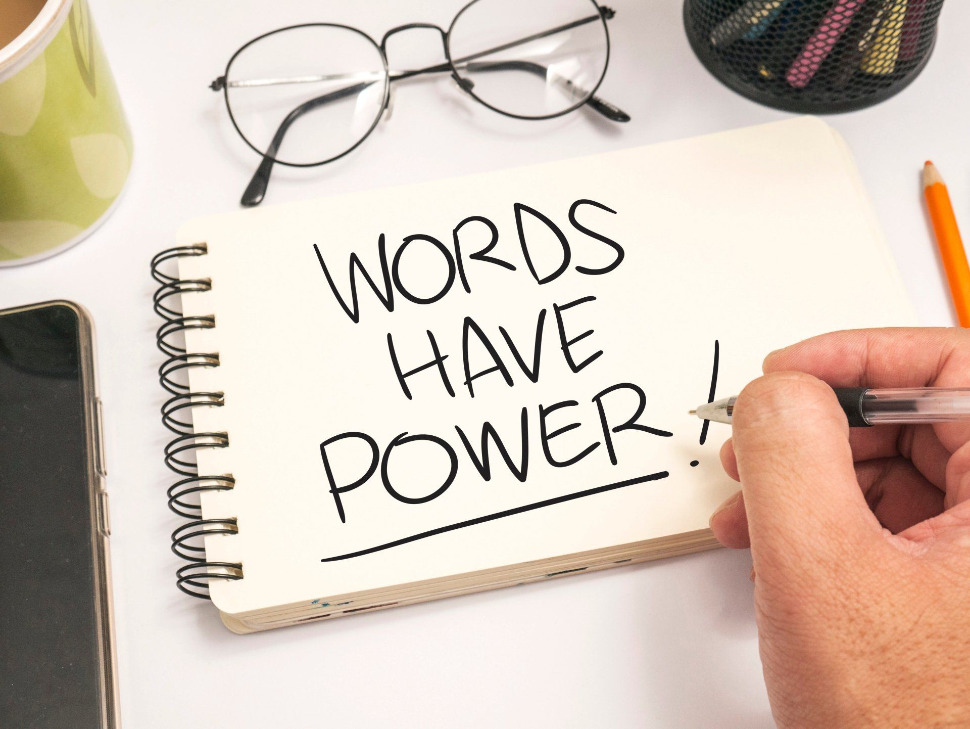 A person is writing in a notebook that says `` words have power ''.