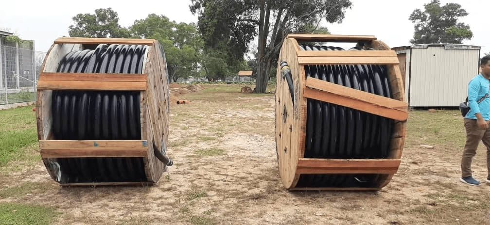 Two wooden spools of black cable on brown ground. Man in teal shirt walks by.