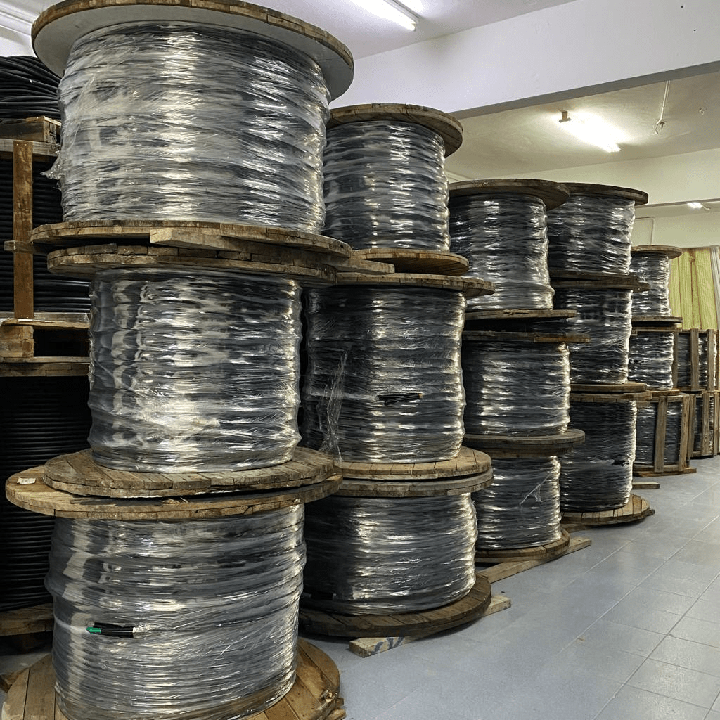 Spools of black cable stacked in a warehouse. Wrapped in plastic, the wooden spools fill a large space.