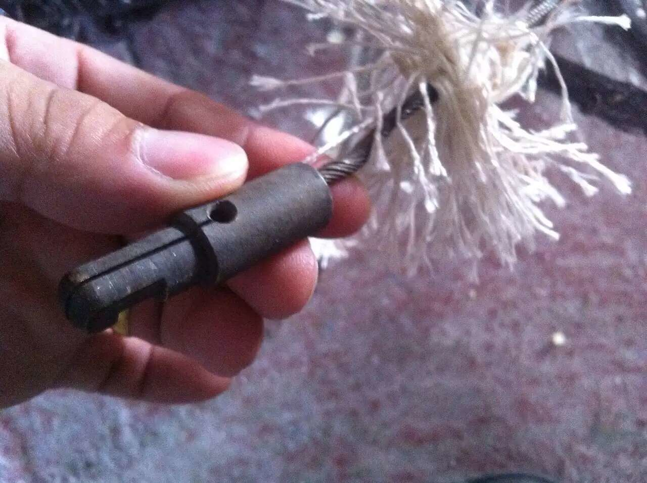 Hand holding a metal tool with a frayed white rope-like brush attached.