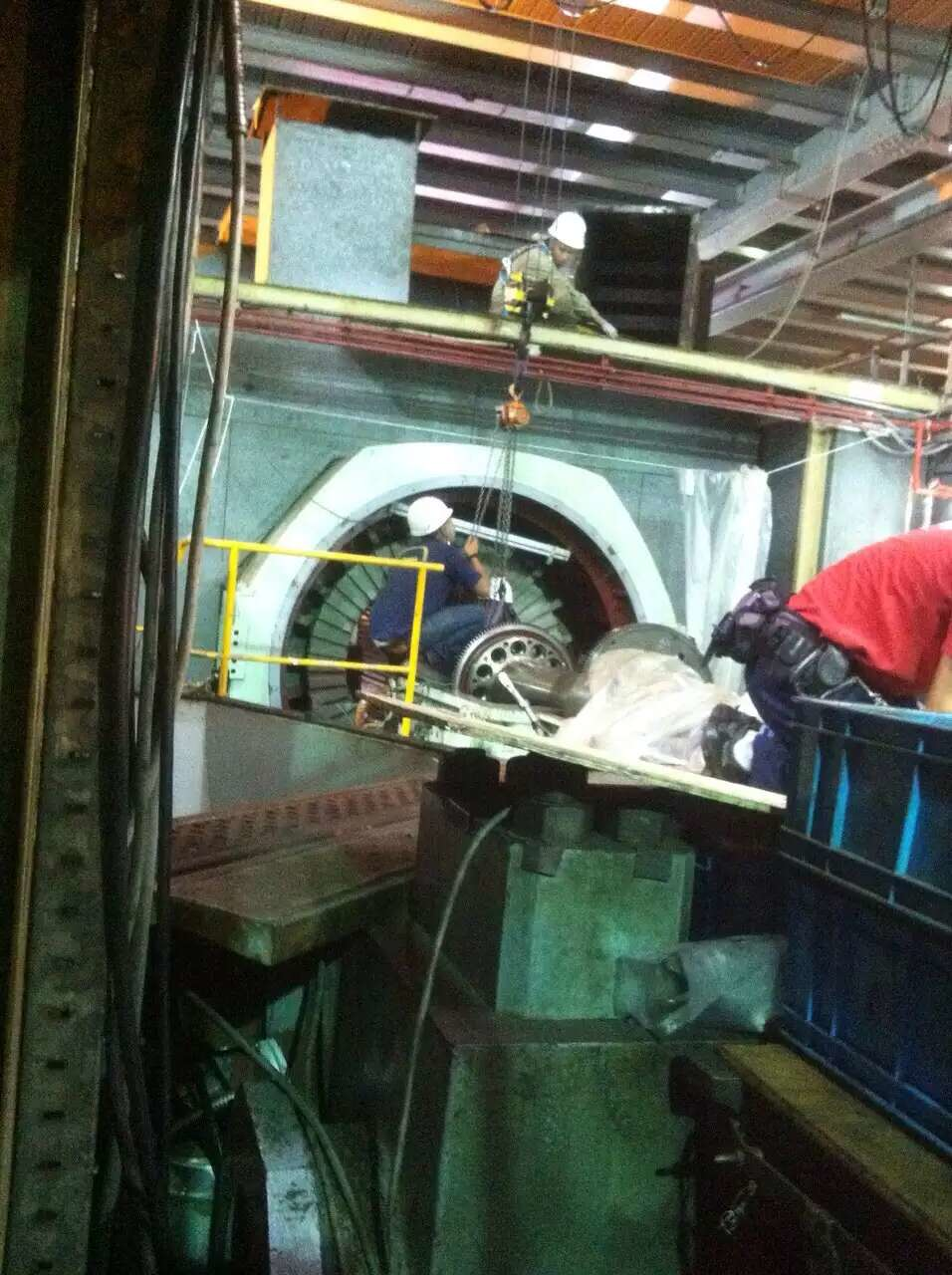 Workers in a factory setting repairing a large industrial machine, utilizing scaffolding and cranes.
