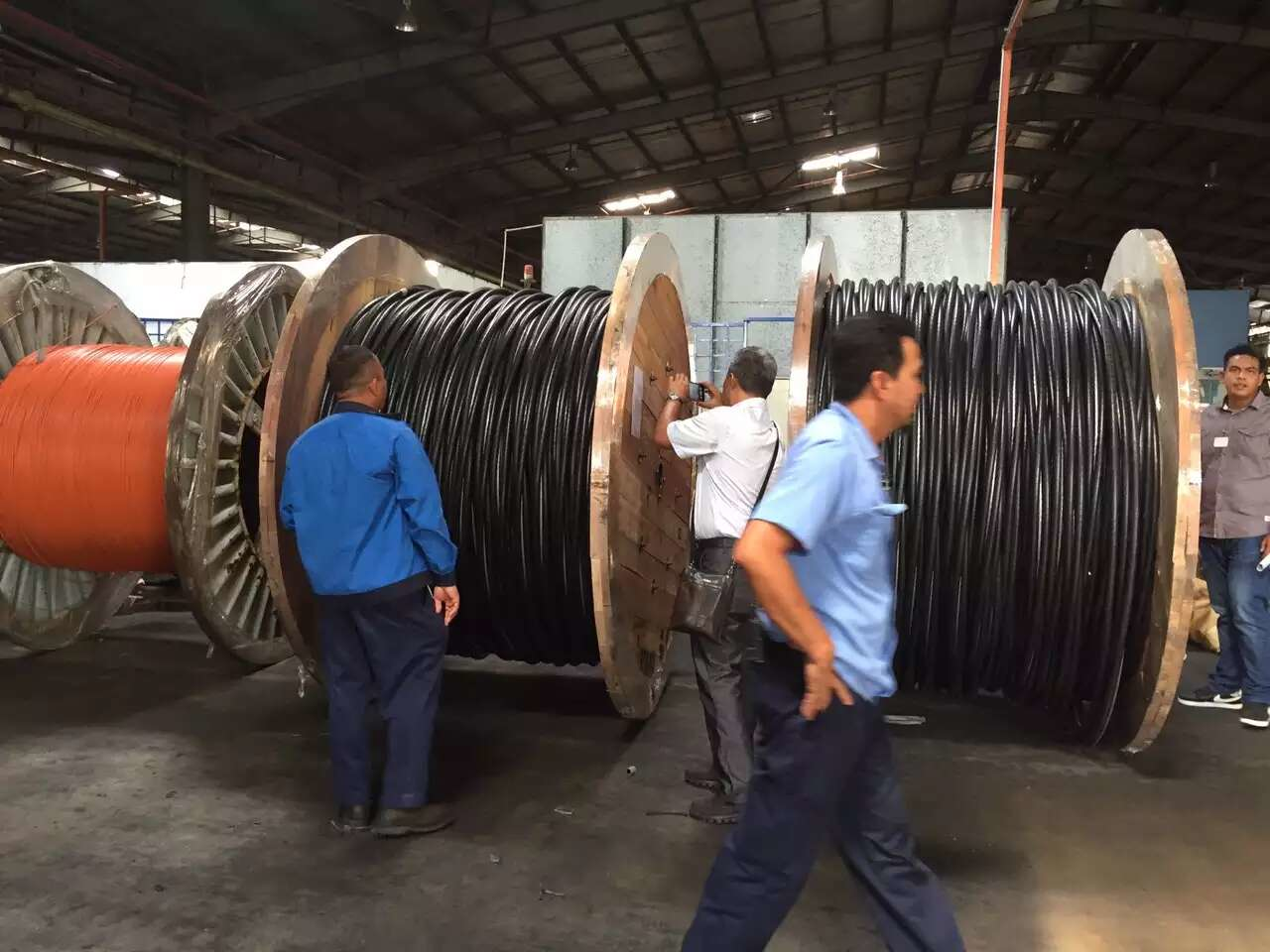 Workers inspecting large spools of black electrical cables inside a factory.