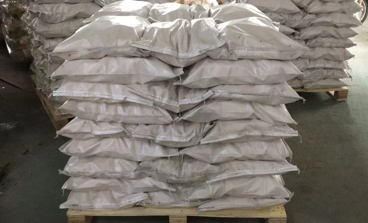 White bags stacked on wooden pallets, possibly in a warehouse.