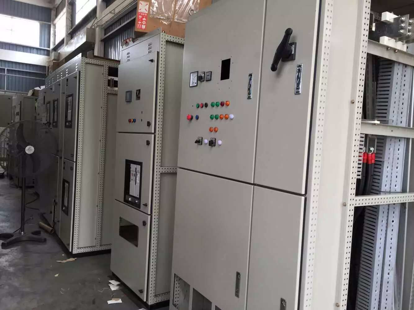 Electrical control panels in a warehouse, varying sizes, gray metal, with buttons, switches, and indicators.