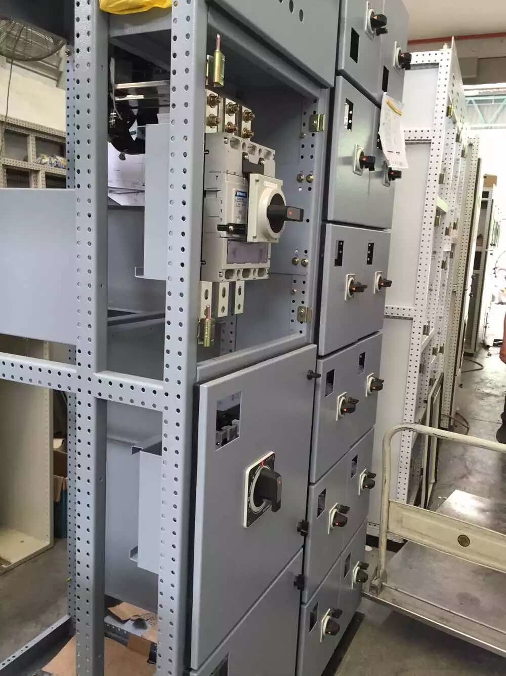 Gray electrical switchgear cabinet with multiple compartments and switches in a workshop.