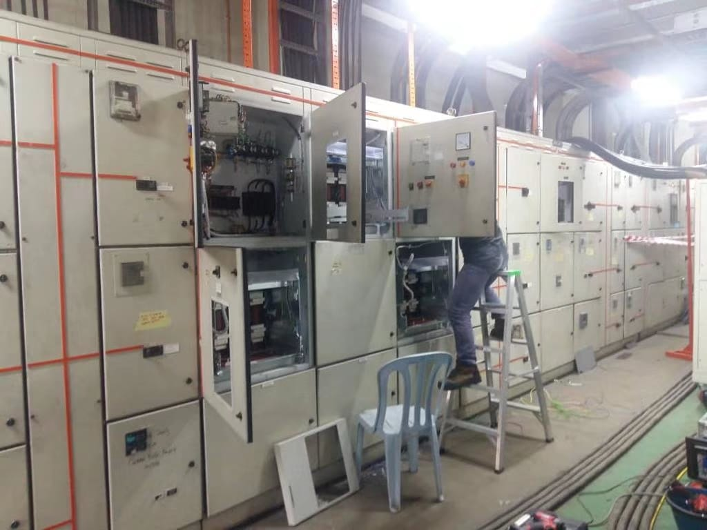 A person on a ladder working inside a large electrical panel in an industrial setting.