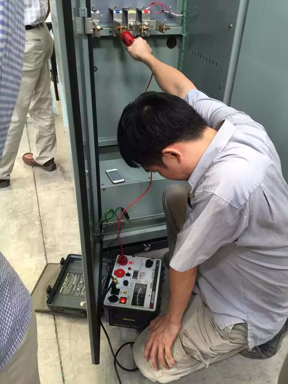 Man testing electrical equipment inside a gray cabinet, using a multimeter.