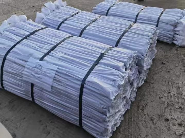 Bundles of white paper sheets, secured with black straps, are stacked outside on a gray surface.