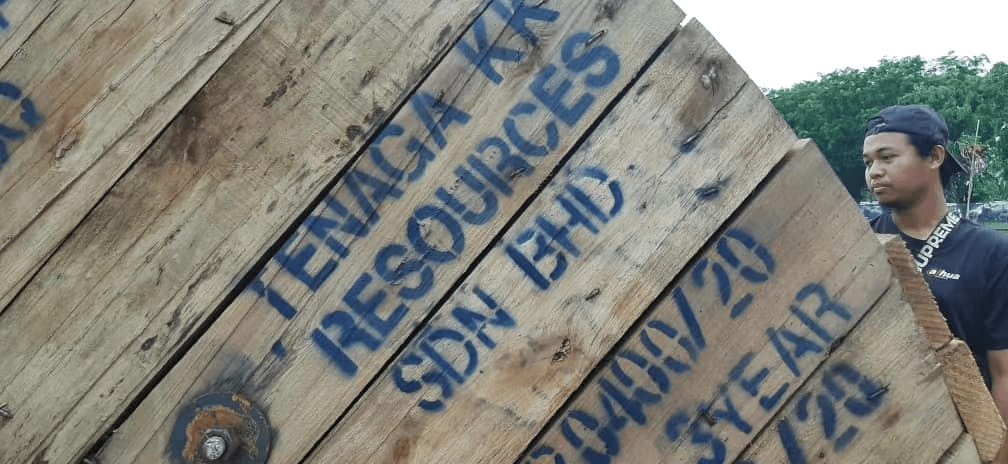 A man looks at a wooden cable spool with blue text that reads 