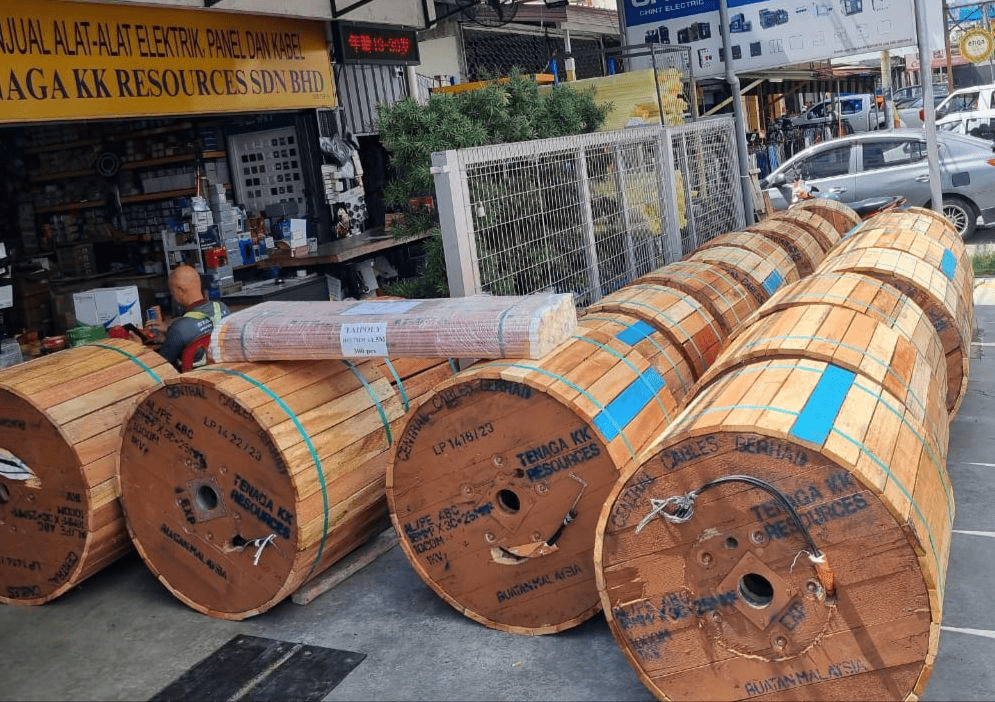 Wooden cable spools lined up on a sidewalk in front of a shop, with cars and a street visible.