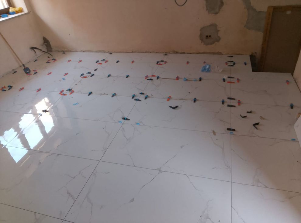 Piastrelle bianche con motivo effetto marmo vengono posate sul pavimento di una stanza, con l'inserimento di distanziatori di livellamento in plastica nelle fughe.