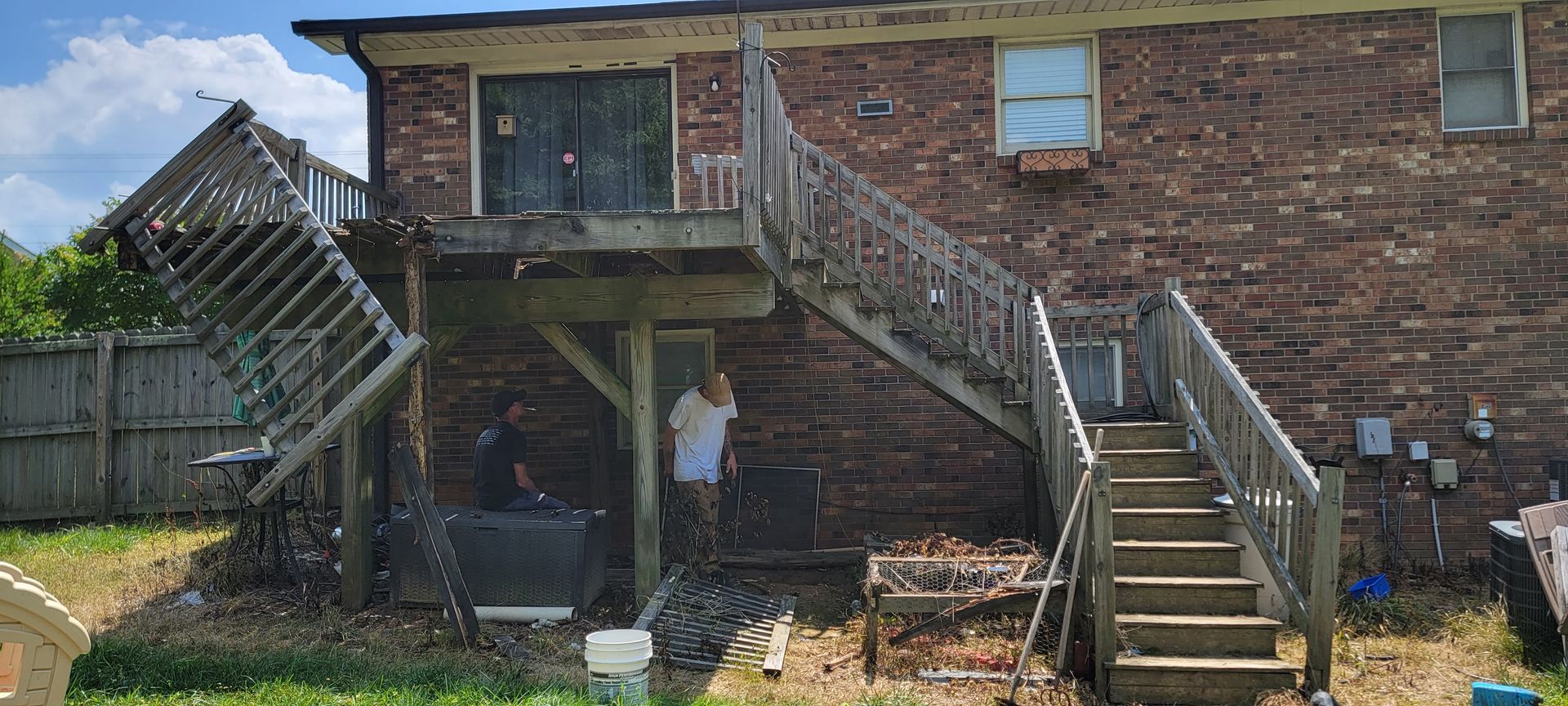 A man is standing in front of a brick house with stairs leading up to it.