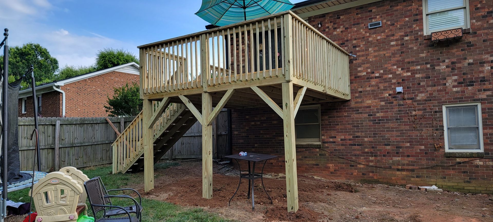 A wooden deck with stairs is in the backyard of a brick house.