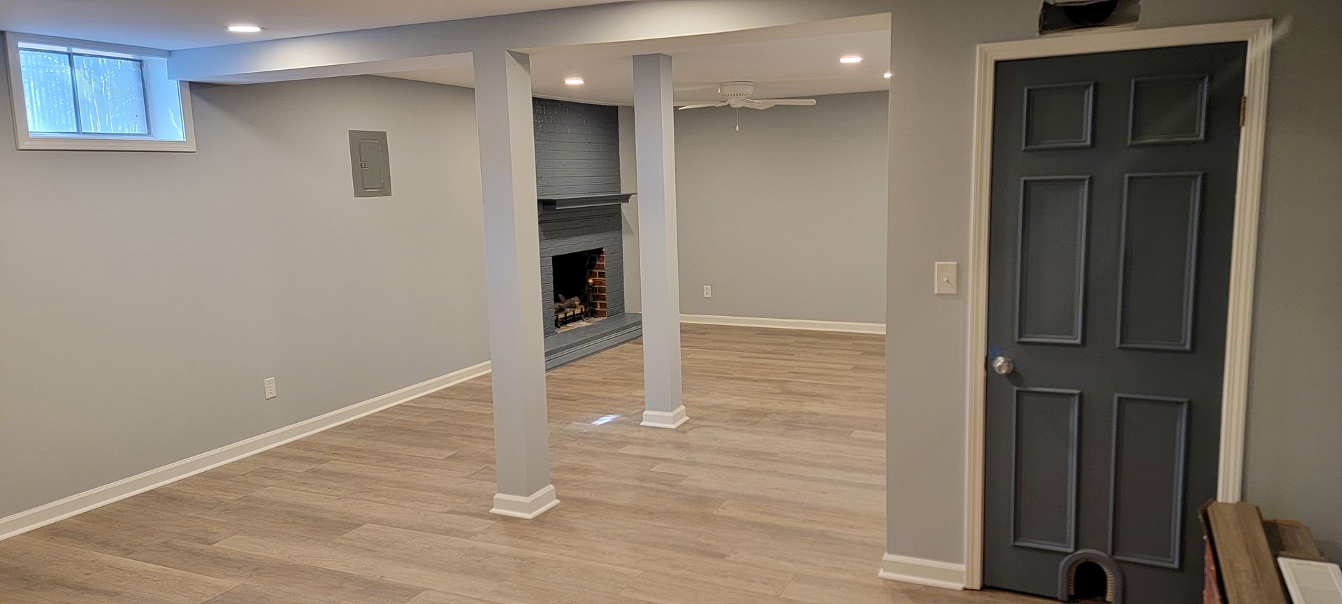 An empty basement with a gray door and a fireplace.