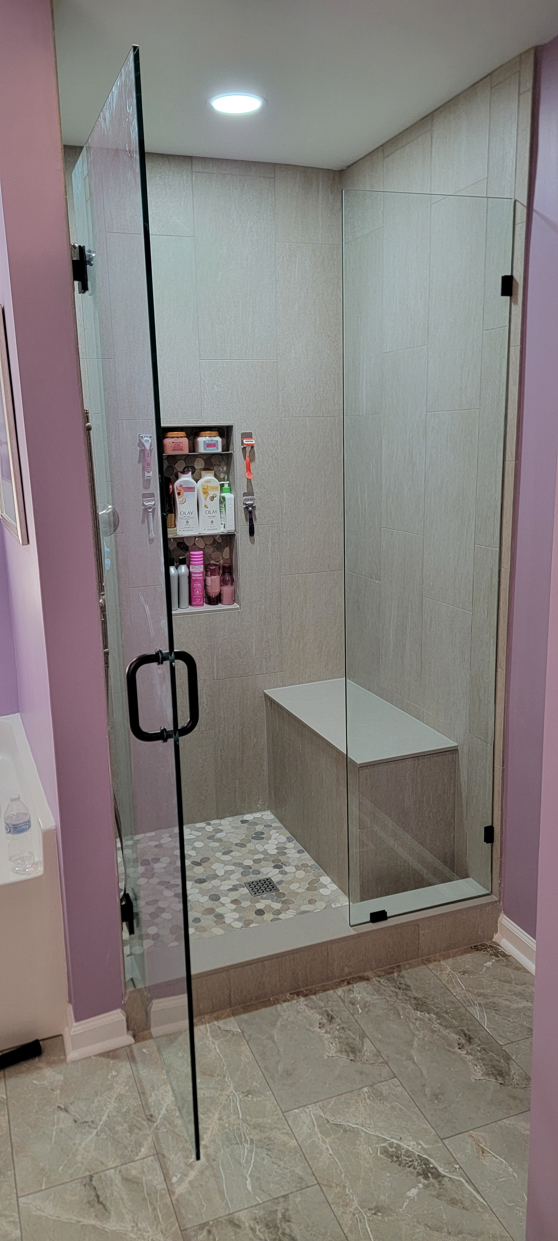 A bathroom with a walk in shower with a glass door and a bench.