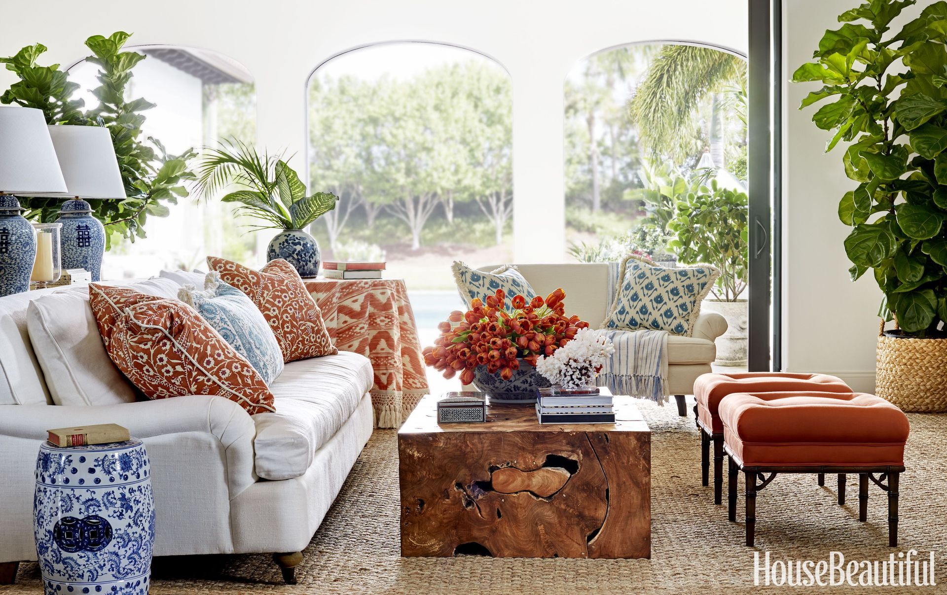 A living room with a couch , coffee table , ottomans and plants.