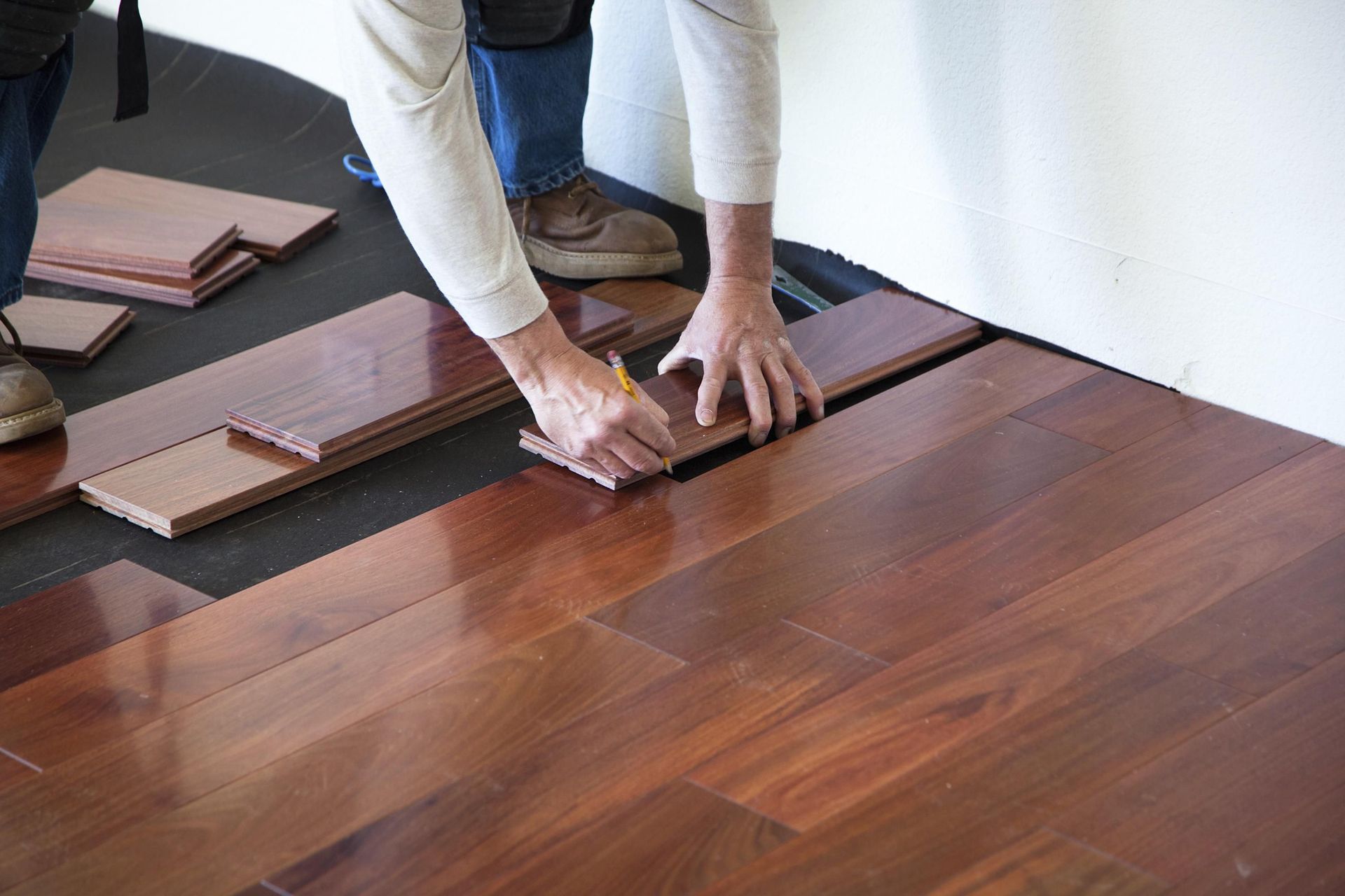 A person is measuring a piece of wood on a hardwood floor.