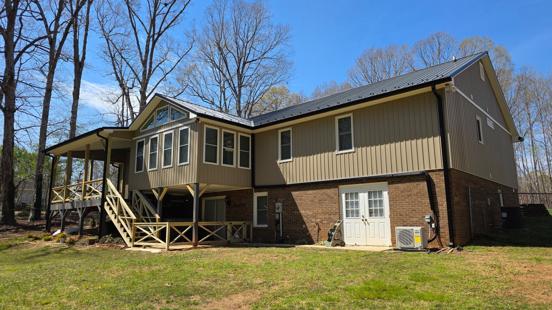 Back of a two-story house with a covered porch, light-colored siding, and a brick foundation, under a bright blue sky.